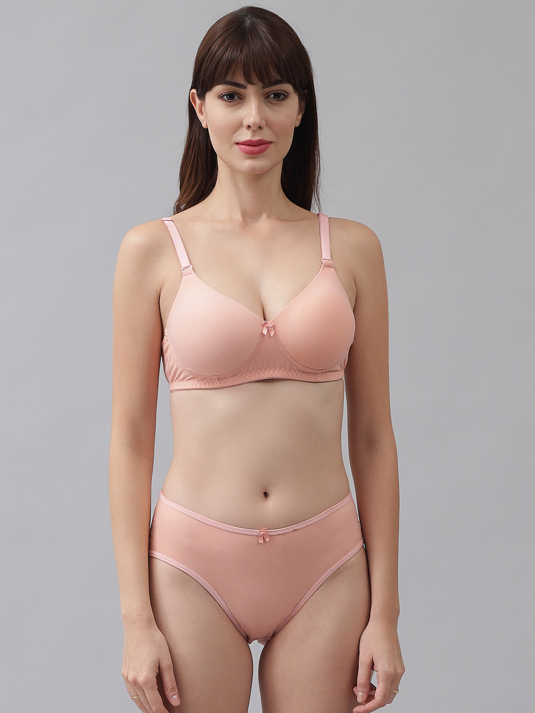 A woman wearing a pink padded lingerie set, which includes a bra and panties, standing against a plain background.